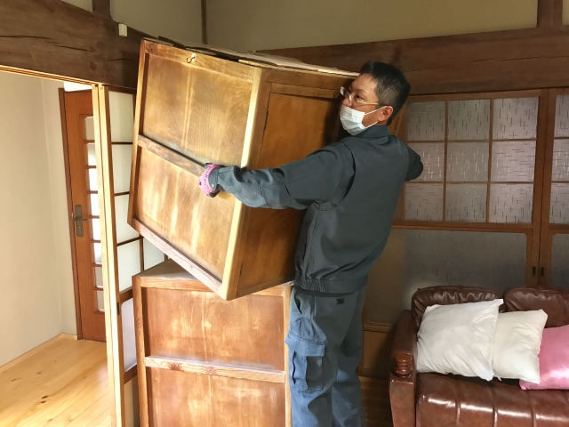 不用品の入った木箱を整理する作業着の男性